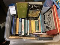 Photo showing a large plastic container filled with a variety of hardcover and paperback books including poetry, westerns, children's books, and art books. Notable titles include 'Complete Love Lyrics' and 'The Sea-Beach at Ebb-Tide.'