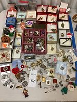 Overview of large assortment of brooch pins laid on table, including boxed and loose pins, varied themes and designs visible