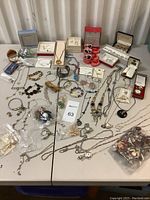 Wide view of all costume jewelry pieces spread on a table with several in boxes, showing variety of necklaces, bracelets, pendants, and boxed sets.