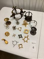 Full view of collection of 17 metal egg stands in varied gold and silver tones, different sizes and unique designs including dragons and floral patterns