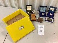 Group view of yellow Lucite box and six mini tape measures in their presentation boxes on tabletop
