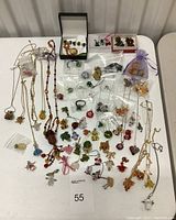 Overview photo showing entire jewelry lot including necklaces, bracelets, pendants, and charms spread on a table.