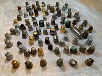 Overview of large assortment of mixed metal and decorative thimbles arranged on cloth.