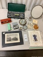 Overview of all items in the lot showing art prints, tools, mirror, glasses, and memorabilia arranged on a white table surface.