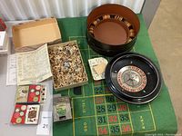 Full view of casino lot with roulette wheel, chips in carrying case, playing cards, puzzle box and pieces, slot machine toy, and betting mat