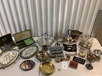 Full table view showing a variety of silver plated trays, platters, candle holders, napkin holders, silverware sets with wooden handles, pitcher, cruet set, toast racks, trinket boxes, and wine stoppers.