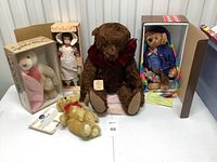 Five collectible teddy bears and porcelain doll arranged on table, showing overall lot content