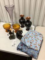 Photo showing all items including large purple vase, two brown bronze tone vases, brown glass bowls, bookends, and fabric material.