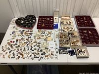 Overview of a large assortment of vintage costume jewelry earrings spread out on a table including boxed and loose pairs.