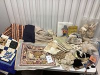 Overview photo showing multiple textile items including blankets, quilt, lace, and book on a white table