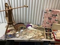 Overview of the table with vintage lace pieces, embroidered fabrics, and the wooden yarn winder and embroidery loop.