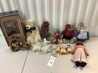 Overview photo of vintage toy collection including teddy bears, plush animals, grandmother doll, and corn husk dolls arranged on a white surface.