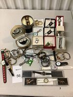 Full overview of all watches on table including boxed and unboxed items, metal, leather, and silicone bands, plus keychain watches