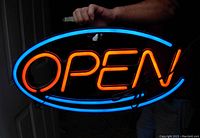 Photo showing the neon-look LED open sign lit up displaying the word 'OPEN' glowing in orange with a blue oval border.