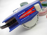 Close-up photo of Dymo Organizer Plus label maker in blue with a black tape loaded with letter dial visible.