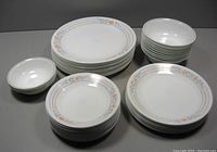 Overview of the full set showing stacks of large plates, salad plates, small plates, bowls, and small bowls with orange floral pattern on the rim.