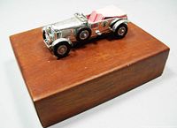 Wooden box with silver British roadster model car mounted on top showing full item.