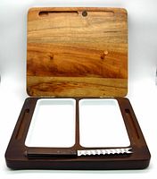 Photo of the folding wooden cheese board in open position showing two white ceramic trays and serrated spreader knife in slot