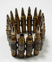 Front view of military dummy practice rounds standing upright in linked belt formation, shows chrome plated bullet tips and brass casings.