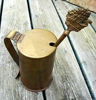 Brass fire starter container with hinged lid and handle, showing ship-topped fire starter tool inserted into the container opening.