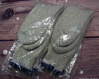 Two pairs of thick wool socks in sealed clear plastic bags laid on a wood surface.