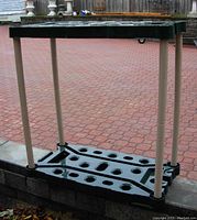 Front view of Rubbermaid storage rack standing on pavement against a brick wall, showing upper and lower shelves with holes for tools