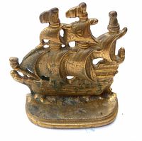 Front view of small solid brass book end shaped like a detailed sailing ship with multiple sails and flags, showing wear and patina.