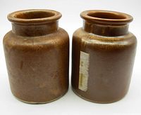 Two brown glazed stoneware mustard pots, side front view showing cylindrical shape and wide mouth rims.