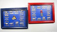Two nautical knots shadow boxes side by side, one with a red frame and miniature lighthouse, the other with a blue frame and brass propeller centerpiece.