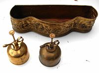 Front view of the brass planter with embossed floral design and two accompanying brass pump misters showing signs of age and use.