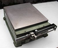 Side angled view of the heavy vintage scale showing silver platform and green base with mechanical sliding weight indicators and metal rods at front.