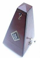 Profile view of the pyramid-shaped wooden metronome with Wittner emblem and winding key on side.