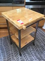 Full view of kitchen cart showing butcher block top, metal frame, lower shelves, and caster wheels.