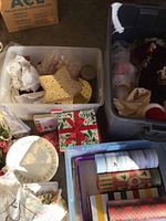 Photo showing three plastic storage tubs filled with various Christmas decor including Santa figurines, gift wrap rolls, holiday boxes, plates, and other holiday decorative items.