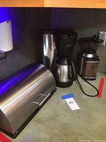 Coffee maker, coffee grinder, and bread box together on a kitchen counter.