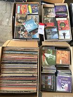 Four cardboard boxes: one packed with vinyl records, three filled with CDs