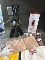Black hand-press juicer placed on kitchen counter with beige cloth, gloves, and boxed Club Crush blender in background