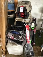 Photo showing two stacked beige plastic pet crates with metal doors, double pet feeders, pet waste scoopers, and packaged pet supplies