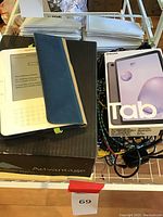 Photo showing Samsung Galaxy Tab A box next to Amazon Kindle with blue sleeve on it, illustrating included items.