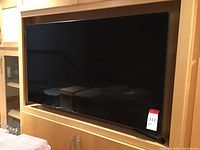 Samsung 55 inch flat screen television mounted on or inset into wooden entertainment unit with reflective black screen turned off.