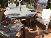 Full view of round gray metal table with two of the four matching chairs visible.