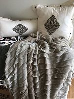 Two cream throw pillows with black embroidered designs with a beige knit throw blanket in front