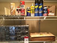 View of multiple spray cans and cleaning product on metal shelving including WD-40, Raid insect spray cans, Scotch Gard, Gum silicone spray, Barbasol shaving cream, and paper towel roll.