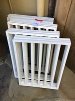 Stack of white foldable dog gate panels placed on a concrete floor.