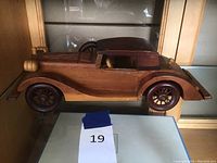 Side view of the wooden model vintage car showing the detailed craftsmanship including wheels and side panels.