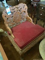 Front view of carved wooden chair with dragon motifs and red velvet cushion.