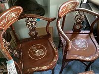 Pair of corner chairs displaying curved arms and inlaid floral motifs on seat and back