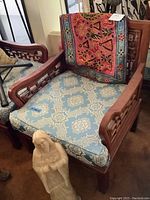 Angled front view showing wood frame, fretwork arms, seat cushion, and draped embroidered textile