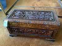 Front view of carved wooden chest showing central Fu Dog motif on top panel and floral carvings on front panel
