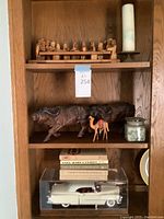 Photo showing last supper sculpture, candle, bison, camel, books, and model car in cabinet